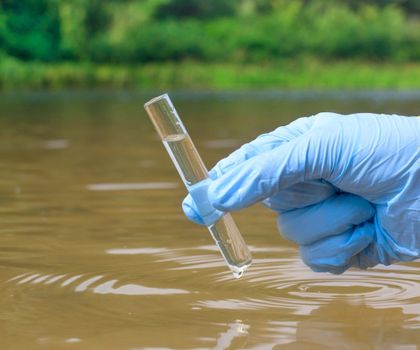 Wasserprobenahme aus einem Fluss (behandschuhte Hand mit Wasserprobe im Glasbehälter)