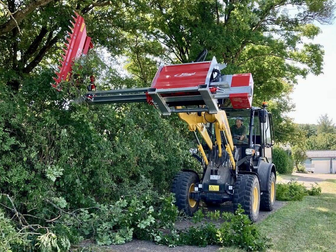 Der Radlader Komatsu WA80M-8 im Einsatz, in dem er mit seinem Anbaugeräte eine Hecke schneidet