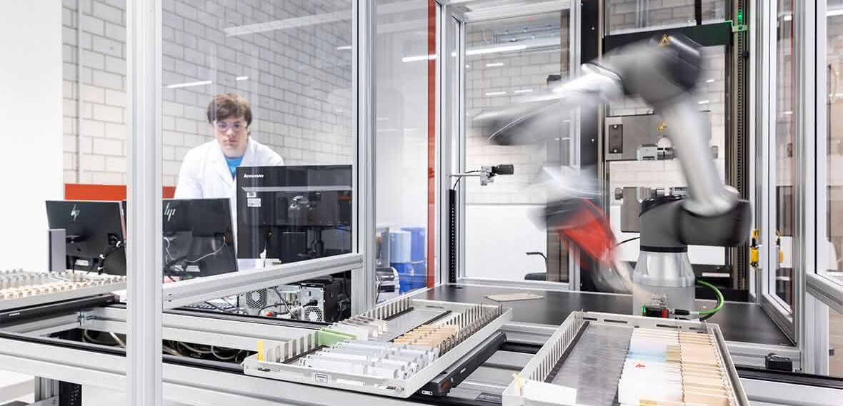 Der Roboterarm befindet sich in einer Einhausung, wo die Probenmagazine über ein Linearschienensystem zugeführt werden.