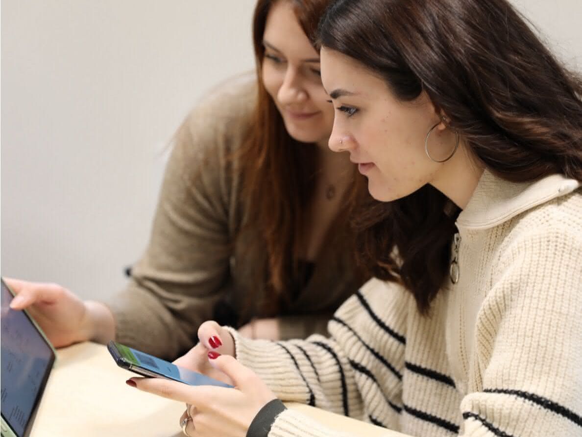 Die Studentinnen legen die Artikel im System an Zwei Studentinnen mit Tablet und Mobile phone