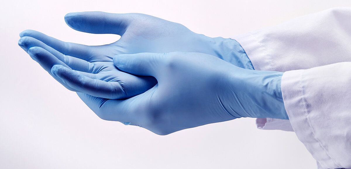 Hände einer Labormitarbeiterin mit blauen LAborhandschuhen