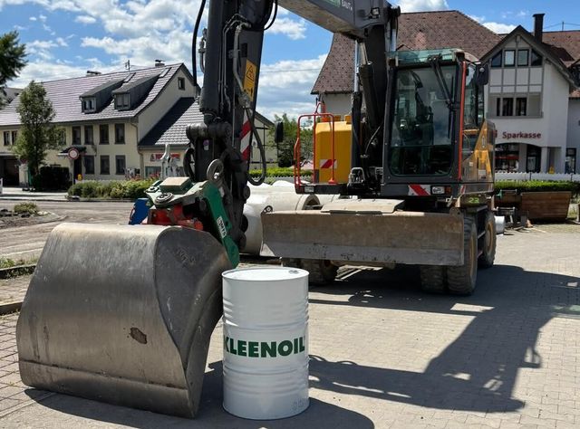 Fass mit Öl von Kleenoil steht Ein Bagger, vor dessen Löffel ein Fass mit Öl von Kleenoil steht