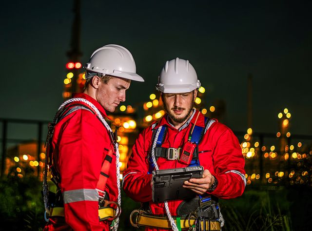 Getac F110 & K120 Tablets: Neue Maßstäbe für Leistung und Zuverlässigkeit Zwei Arbeiter stehen nachts in roten Schutzanzügen auf einer Baustelle und lesen auf einem Getac-Tablet