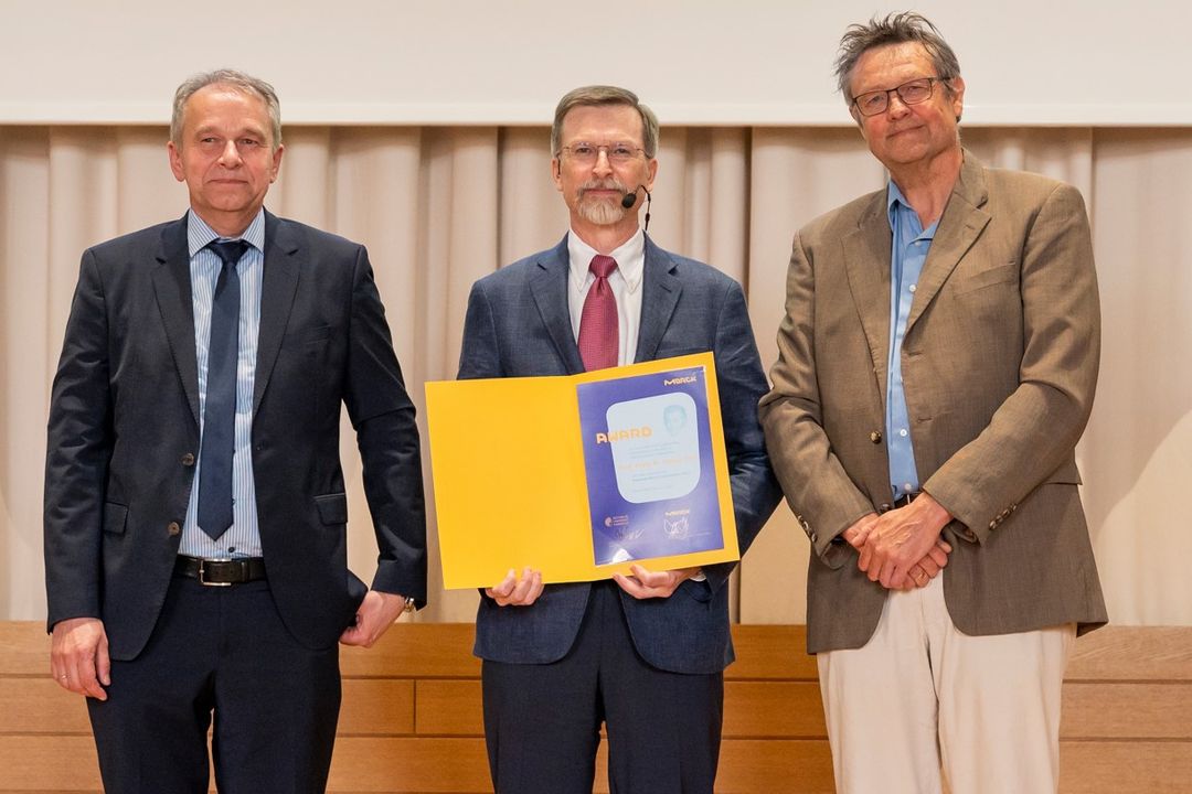 Ulrich Betz und Professor Felix Hausch vom Fachbereich Chemie der TU Darmstadt überreichten Craig M. Crews die Auszeichnung