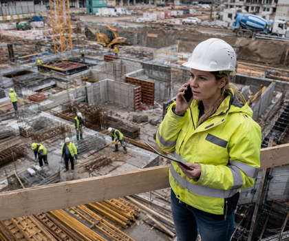 Eine Bauleitern spricht sorgenvoll auf einer Baustelle in ihr Smartphone