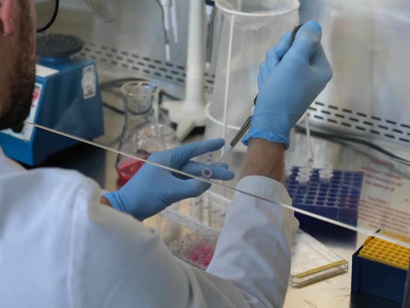 Durch gezielte Optimierung der Arbeitsabläufe kann ein große Menge an Kunststoffabfällen im Labor reduziert werden. Labormitarbeiter beim Pipettieren hinter einer Glaswand