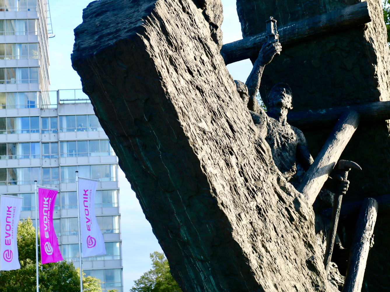 Evonik baut Tausende Stellen ab - Warum das ein Warnsignal für die Chemiebranche ist Evonik Firmengebäude im Hintergrund mit Statue im Vordergrund, die einen Arbeiter Bergbau darstellt