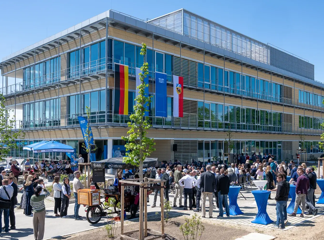 Zentrum für Infektionsprävention: Neuer Forschungsbau an der TUM eröffnet. Das Zentrum für Infektionsprävention (ZIP) steht am Campus Freising-Weihenstephan und ist Teil der TUM School of Life Sciences. Unter Leitung des wissenschaftlichen Direktors Dietmar Zehn wird hier unter anderem zu multiresistenten Keimen geforscht. Ein Gebäude mit vielen Fenstern und Glasfassade ist zu sehen. Im Vordergrund stehen viele Menschentrauben vor dem Gebäude, geschart um Stehtische und junge Bäume. An der Fassade hängen die Flaggen Deutschlands, Bayerns, der TUM und der Stadt Freising.