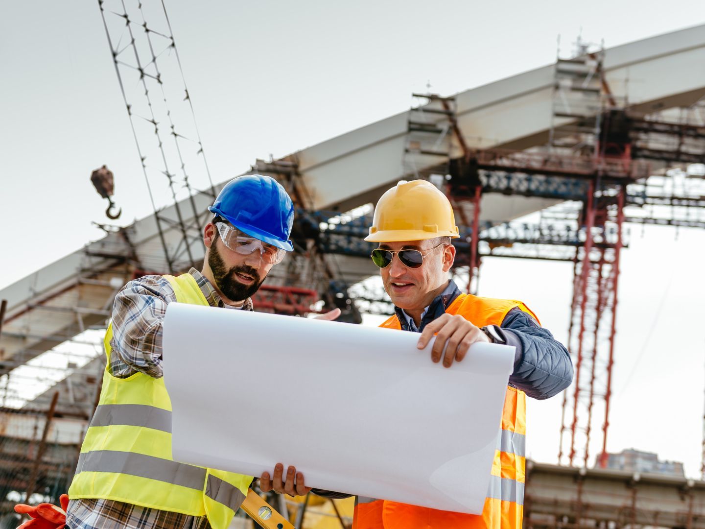 Zwei Arbeiter betrachten einen Bauplan vor der Baustelle einer Brücke