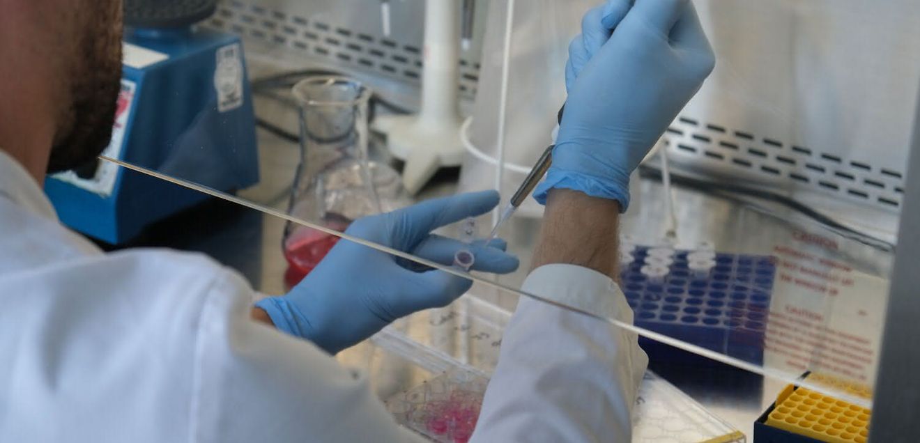 Durch gezielte Optimierung der Arbeitsabläufe kann ein große Menge an Kunststoffabfällen im Labor reduziert werden. Labormitarbeiter beim Pipettieren hinter einer Glaswand