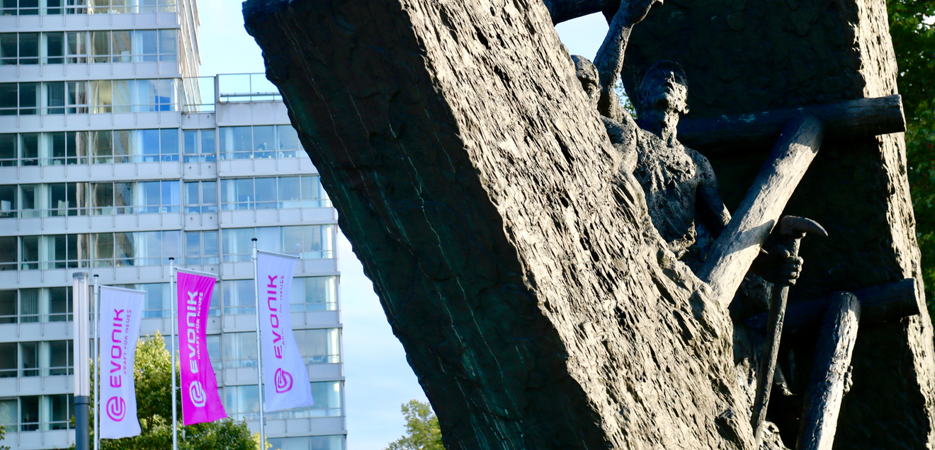 Evonik baut Tausende Stellen ab - Warum das ein Warnsignal für die Chemiebranche ist Evonik Firmengebäude im Hintergrund mit Statue im Vordergrund, die einen Arbeiter Bergbau darstellt