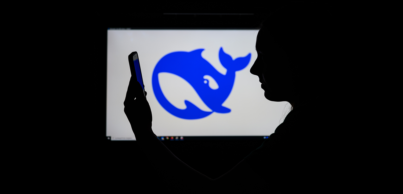 Das Logo des chinesischen KI-Start-ups DeepSeek auf einem Computerbildschirm zu sehen, während davor eine Frau auf ihr Smartphone schaut.