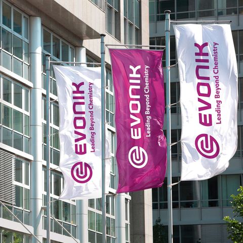 Evonik überrascht mit Ergebnisplus und hält dennoch an Stellenabbau fest Evonik Firmengebäudeim Hintergrund, davor Flaggen in weiß und magenta mit der Aufschrift Evonik und dem Firmenlogo