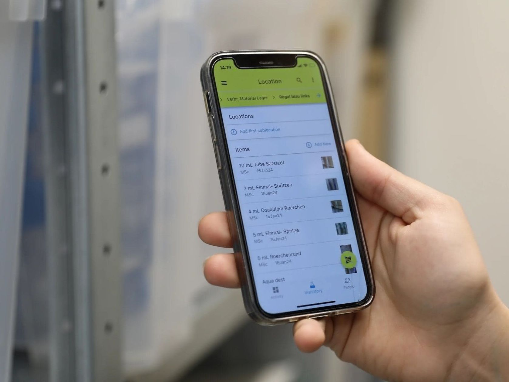 Digitalisierung von Laborbeständen und Lagerorten Studierende im Ausbildungslabor hält ein Mobiltelefon in der Hand, auf dem Lagerbestände der Labor-Materialien und Bestände der Chemikalien im Labor angezeigt werden.