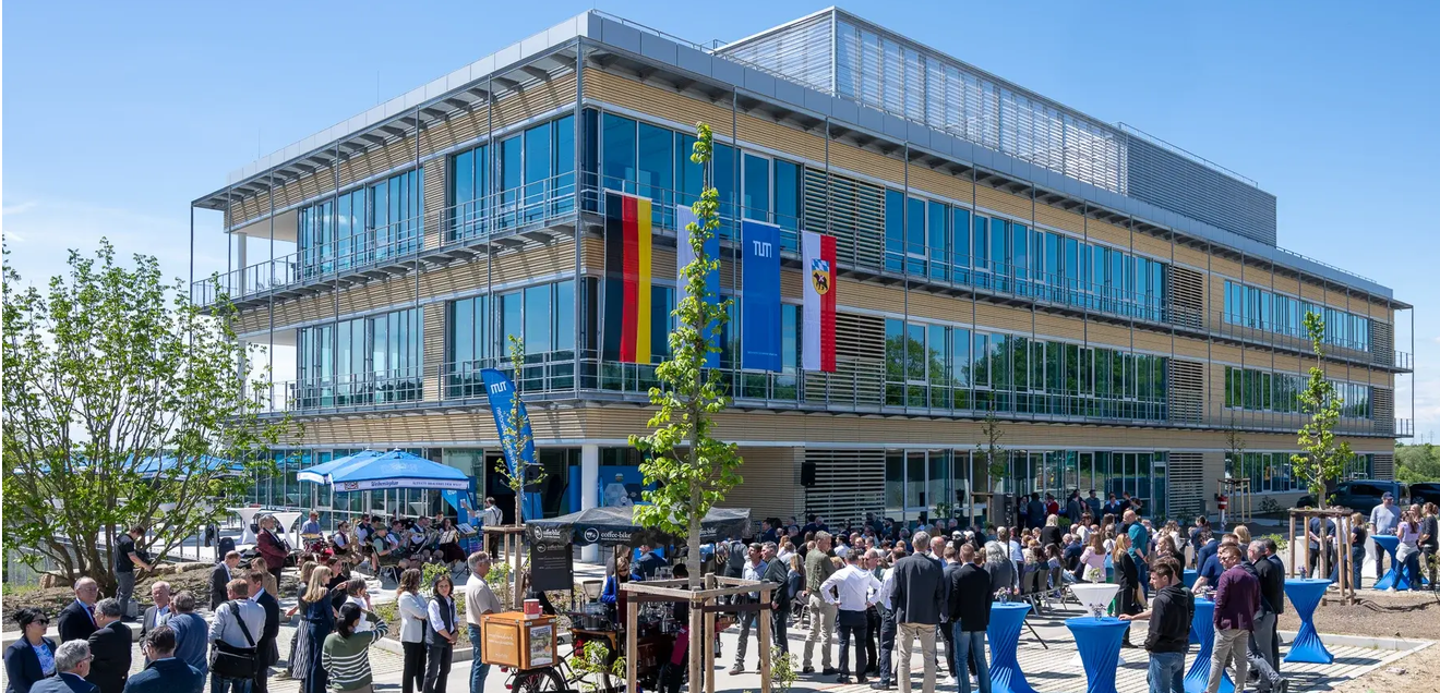 Zentrum für Infektionsprävention: Neuer Forschungsbau an der TUM eröffnet. Das Zentrum für Infektionsprävention (ZIP) steht am Campus Freising-Weihenstephan und ist Teil der TUM School of Life Sciences. Unter Leitung des wissenschaftlichen Direktors Dietmar Zehn wird hier unter anderem zu multiresistenten Keimen geforscht. Ein Gebäude mit vielen Fenstern und Glasfassade ist zu sehen. Im Vordergrund stehen viele Menschentrauben vor dem Gebäude, geschart um Stehtische und junge Bäume. An der Fassade hängen die Flaggen Deutschlands, Bayerns, der TUM und der Stadt Freising.