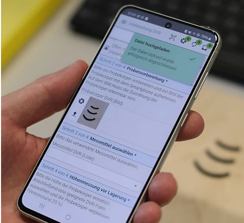 Handy in der Hand eines Labormitarbeitenden