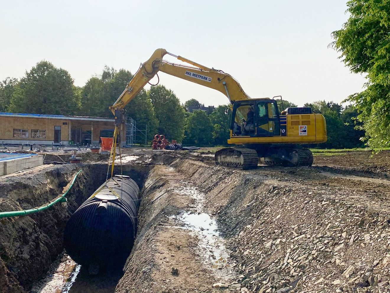 Ein Bagger von HKL Baumaschinen setzt ein Rohr in einen Graben