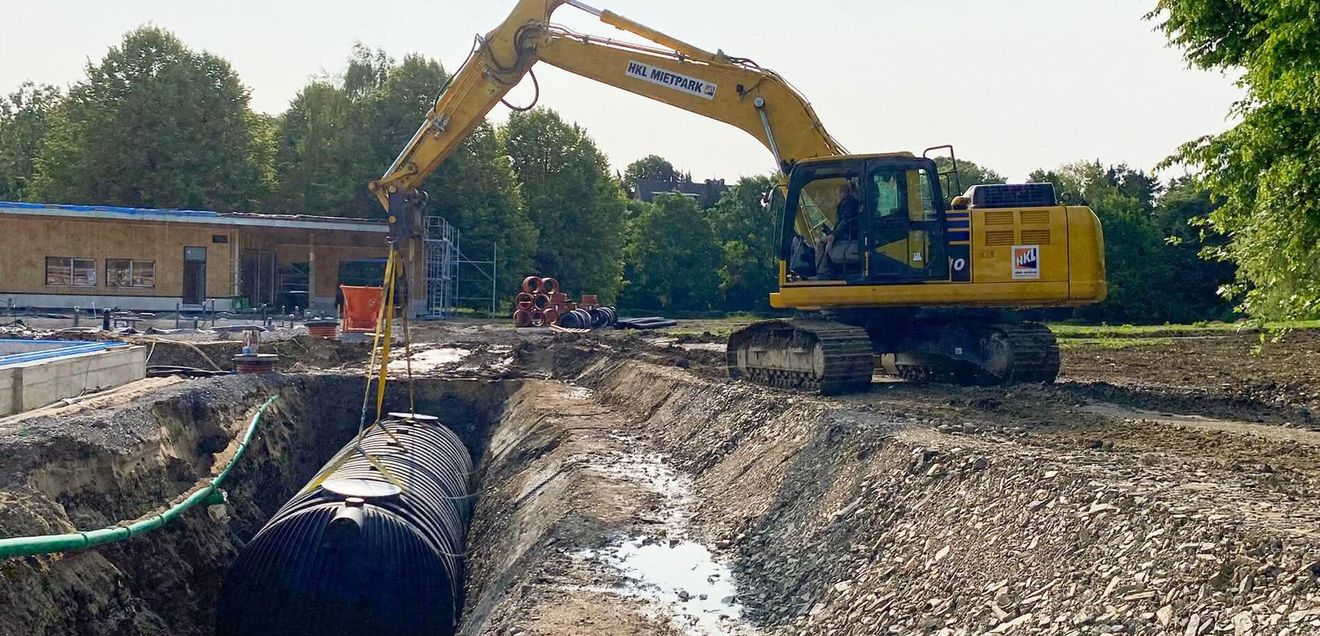 HKL Bagger Ein Bagger von HKL Baumaschinen setzt ein Rohr in einen Graben