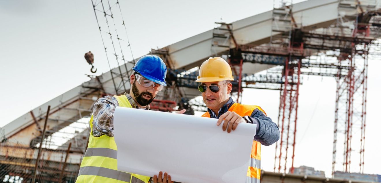 Frankreich - Innovationen für das Baugewerbe Zwei Arbeiter betrachten einen Bauplan vor der Baustelle einer Brücke