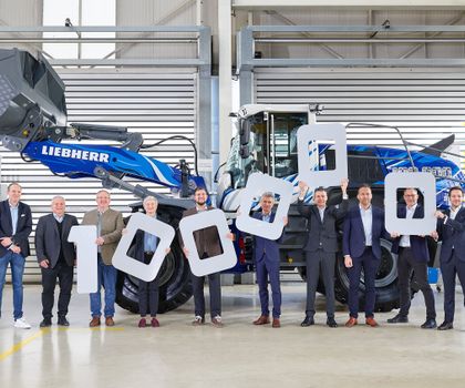 Übergabe Radlader Liebherr Gruppenbild mit den Vertretern aller beteiligten Firmen in einer Werkshalle vor dem Liebherr-Radlader mit blau-weißer Lackierung