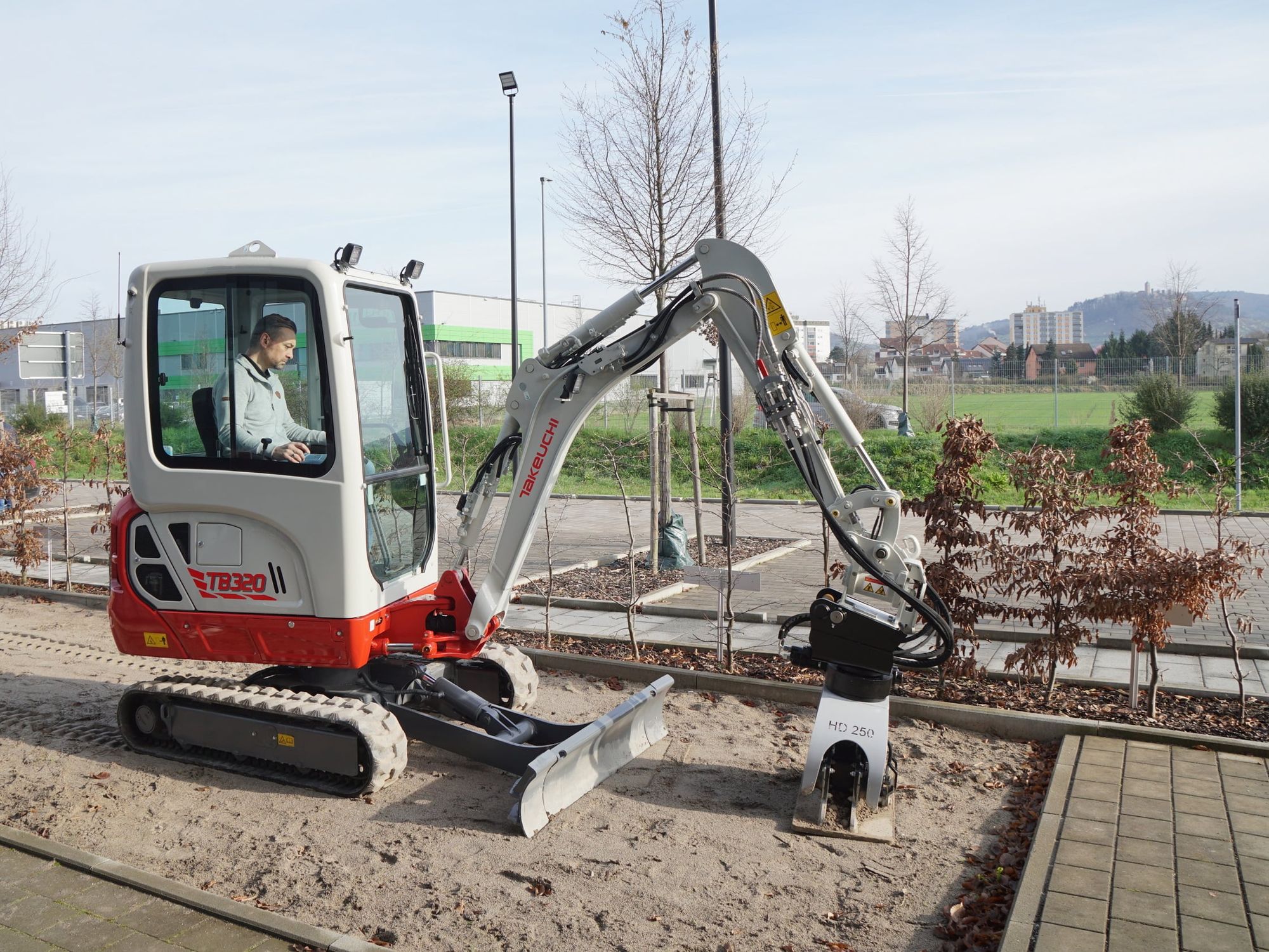Ein Takeuchi Kompaktbagger TB 320 im typisch rot-weißem Anstrich, der Pflastersteine verlegt