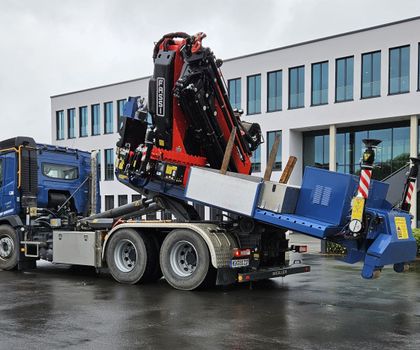 Ladekran von Fassi auf Abrollcontainer-Chassis Der Fassi F7 10RA.2.28 xhe-dynamic auf dem Abroll-Chassis vor einem Werksgebäude