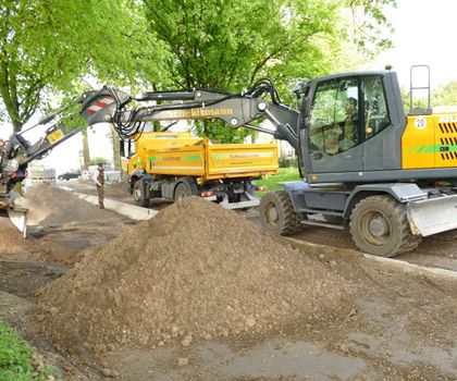Atlas 165 W: Effizienter Mobilbagger für anspruchsvolle Bauprojekte Ein Atlas 165 W befüllt einen Lastwagen mit Material einer Baustelle am Bankett einer Allee