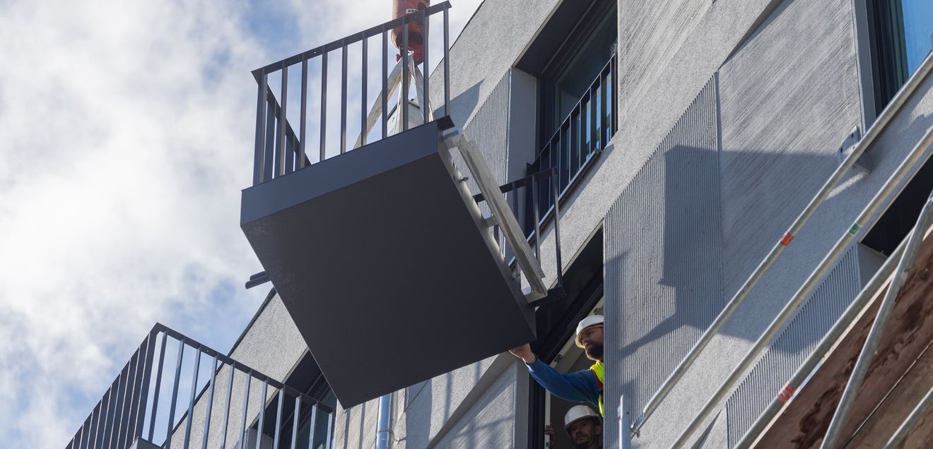 Ein Balkon wird vom Kran an die Fassade gehoben. Die Montage konnte schnell und aufgrund der hohen Wiederholungsrate sehr zeiteffizient erfolgen. Ein Balkon wird vom Kran an die Fassade gehoben. Die Montage konnte schnell und aufgrund der hohen Wiederholungsrate sehr zeiteffizient erfolgen.
