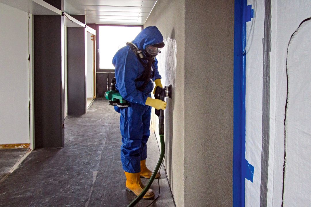 Ein Facharbeiter in Schutzanzug und Atemschutzmaske entfernt den Putz von der Wand Ein Facharbeiter in Schutzanzug und Atemschutzmaske entfernt den Putz von der Wand