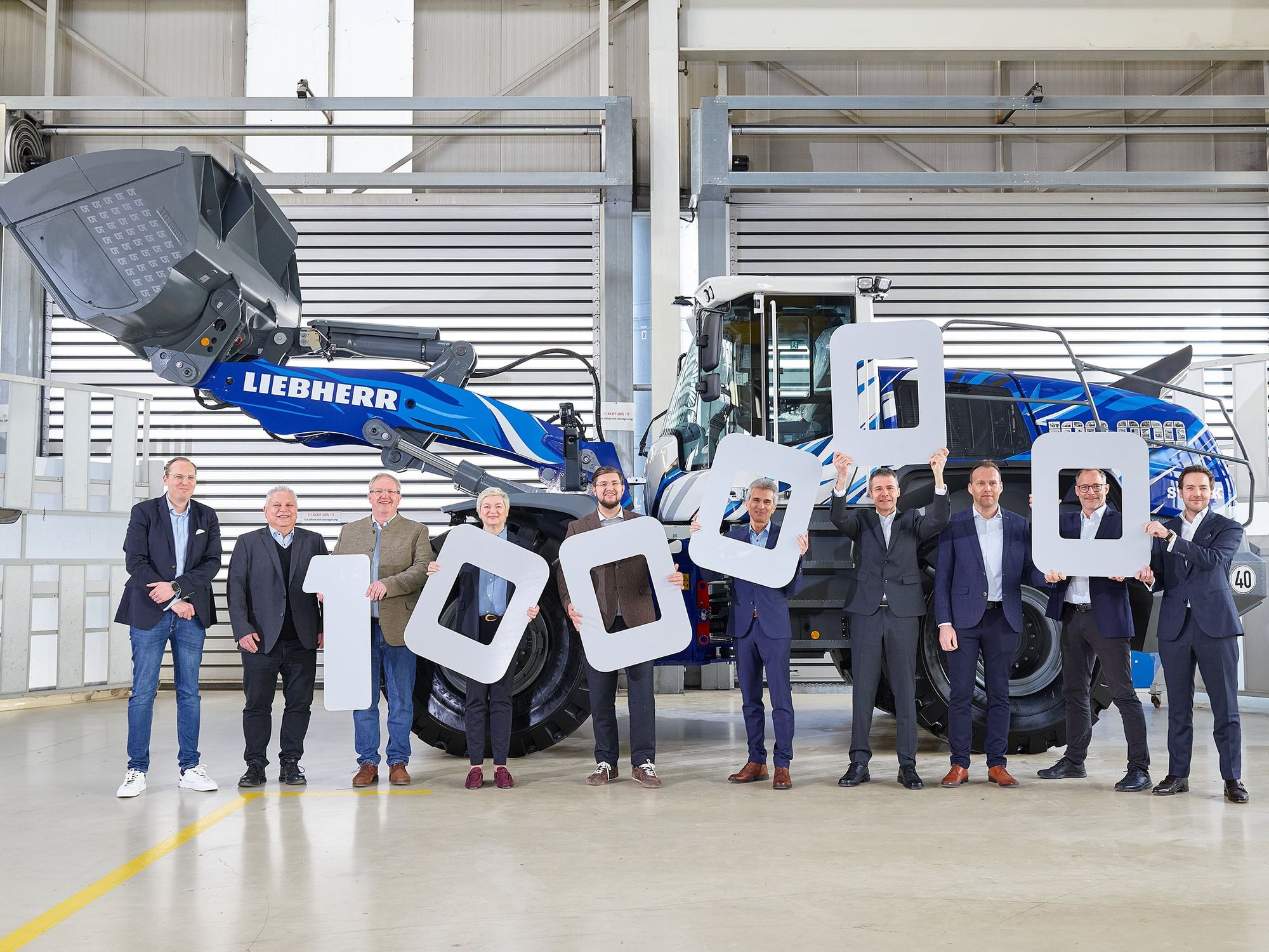Übergabe Radlader Liebherr Gruppenbild mit den Vertretern aller beteiligten Firmen in einer Werkshalle vor dem Liebherr-Radlader mit blau-weißer Lackierung