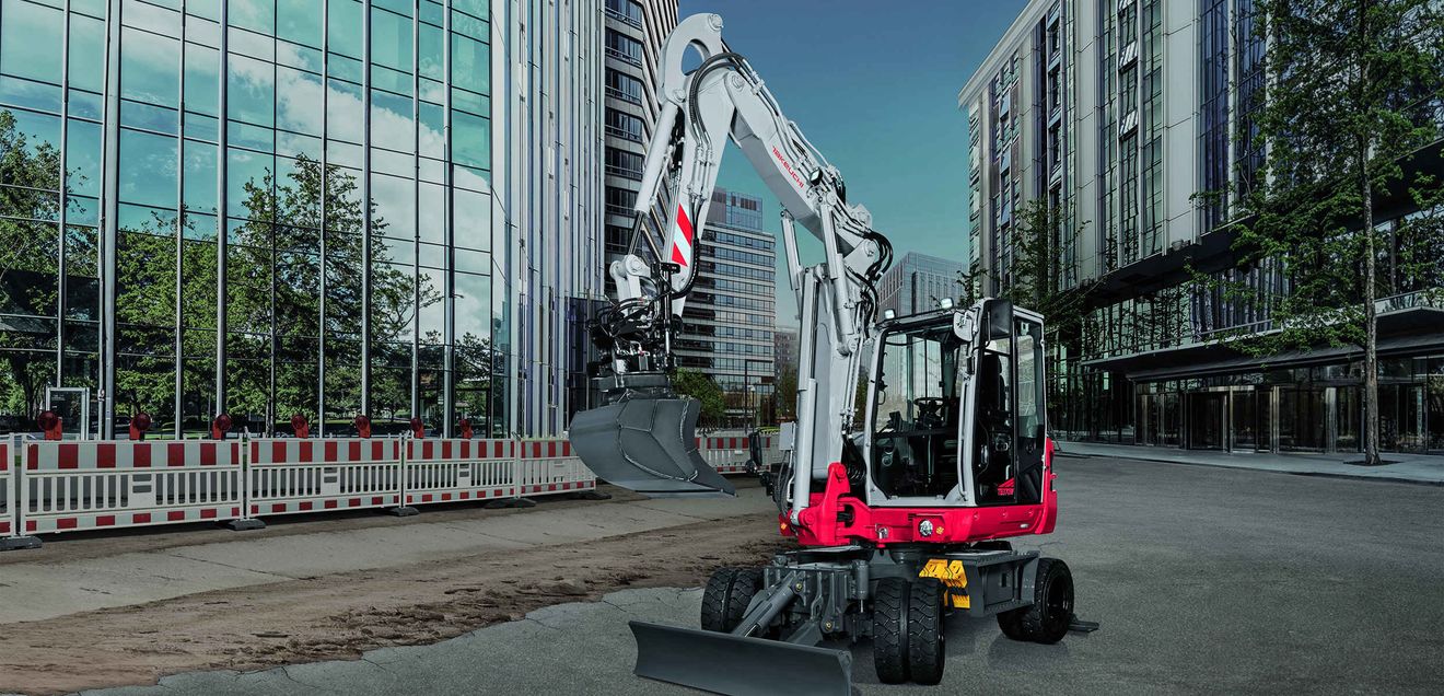 Ein neuer Takeuchi TB 370W vor mehreren Hochäusern mit Glasfassaden