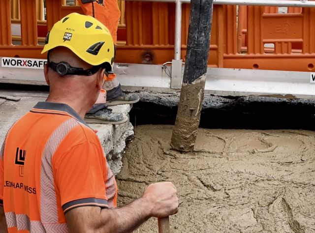 Ein Arbeiter beobachtet, wie Beton in eine Baugrube läuft