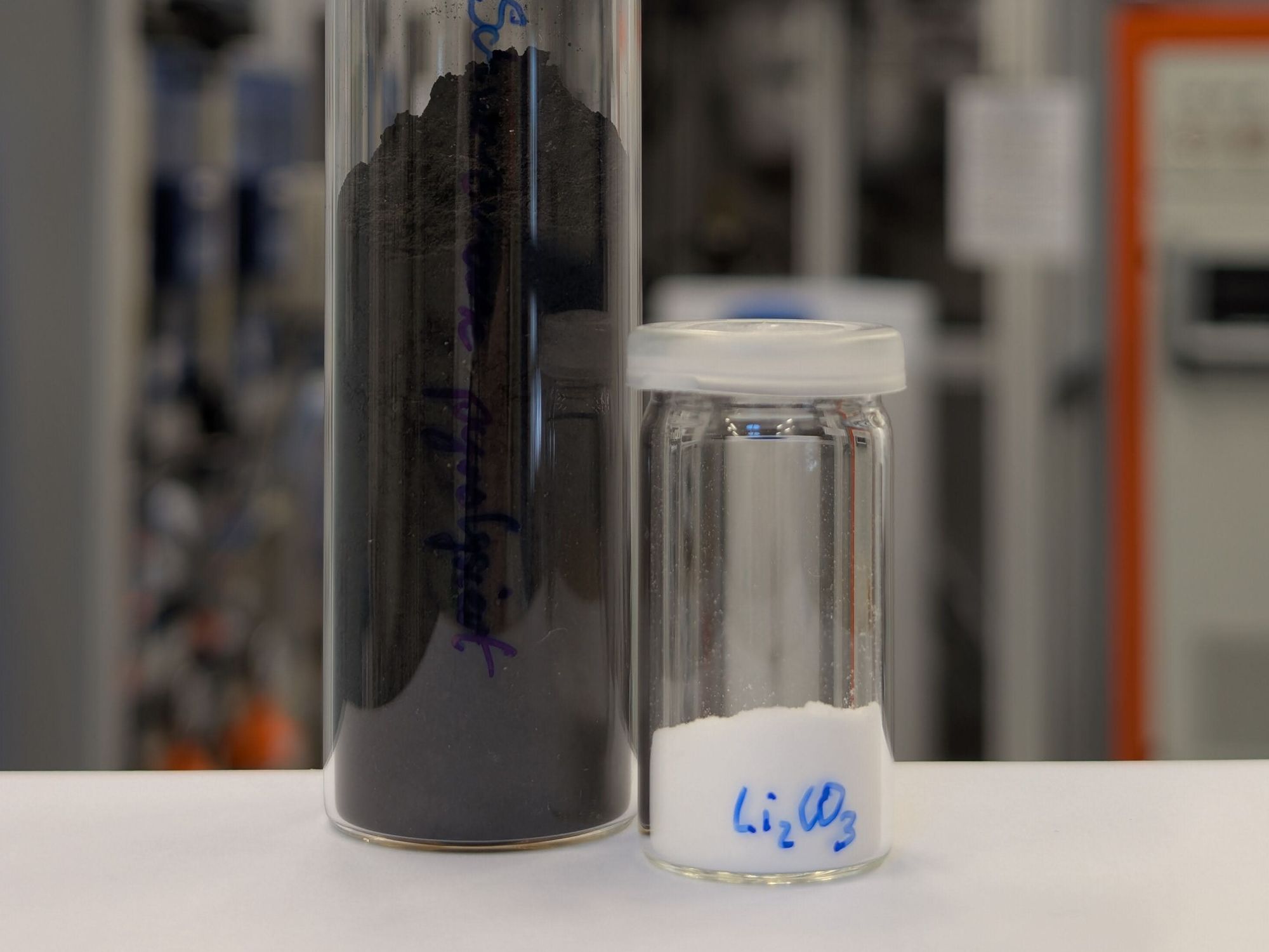 Schwarzmasse aus Lithium-Ionen-Batterien und daraus extrahiertes Lithiumcarbonat Zwei Glasgefäße: Eines enthält Schwarzmasse und das zweite weißes Lithiumcarbonat