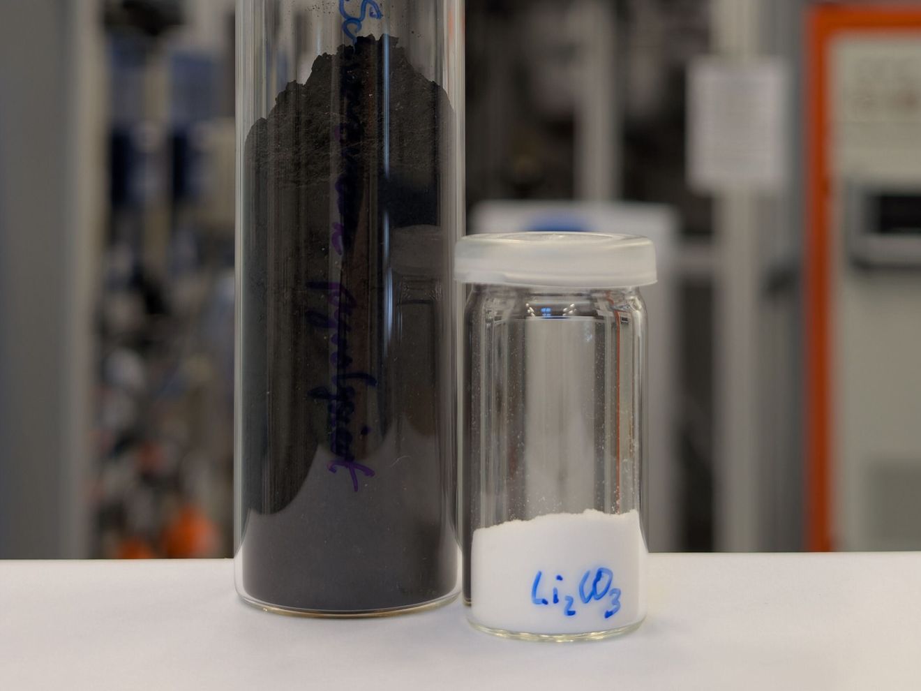 Schwarzmasse aus Lithium-Ionen-Batterien und daraus extrahiertes Lithiumcarbonat Zwei Glasgefäße: Eines enthält Schwarzmasse und das zweite weißes Lithiumcarbonat