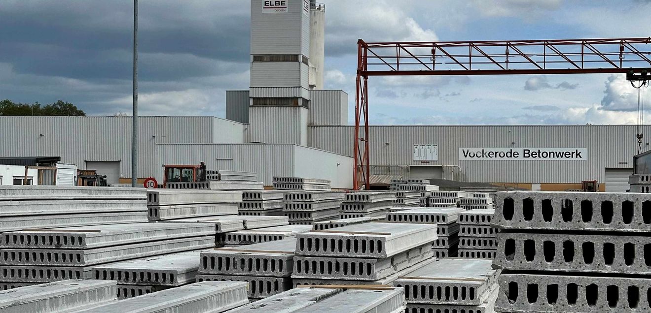 Betonelemente liegen auf einer Lagerstätte. Im Hintergrund ein großes Gewerbegebäude mit ELBE-Logo