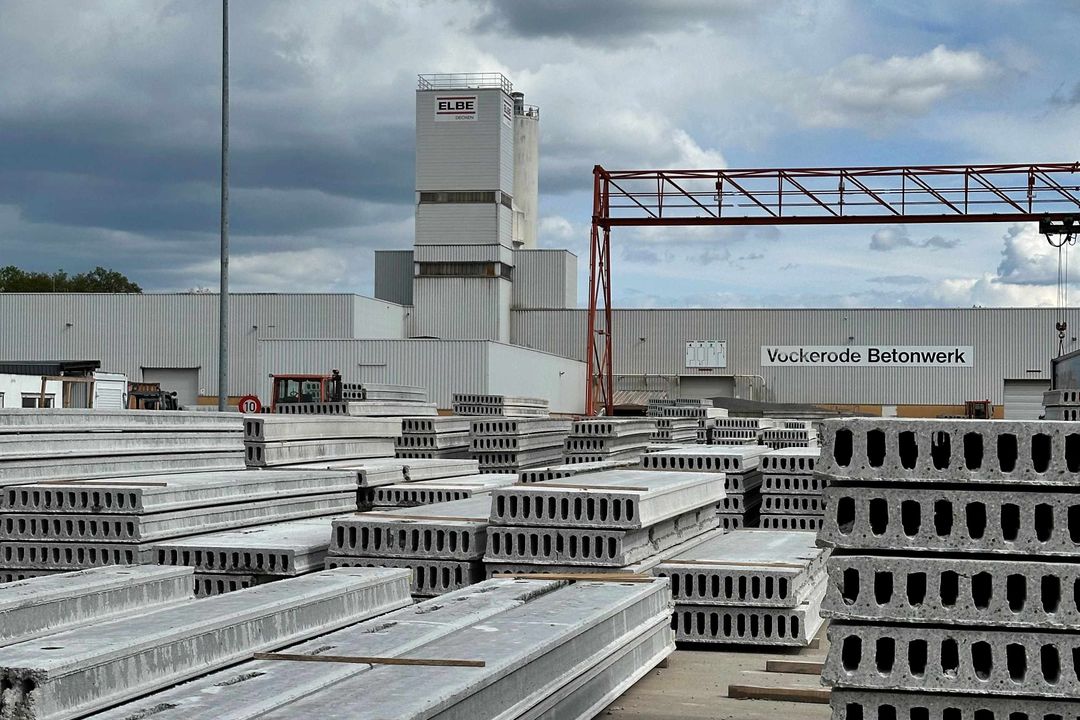Betonelemente liegen auf einer Lagerstätte. Im Hintergrund ein großes Gewerbegebäude mit ELBE-Logo