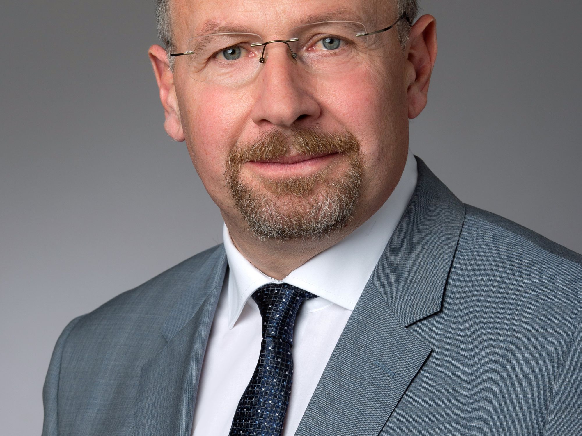 Friedrich Mozelt, Geschäftführer von Kuhn Baumaschinen. Friedrich Mozelt, Geschäftführer von Kuhn Baumaschinen, lächelt freundlich in die Kamera und trägt einen grauen Anzug mit schwarzer Krawatte