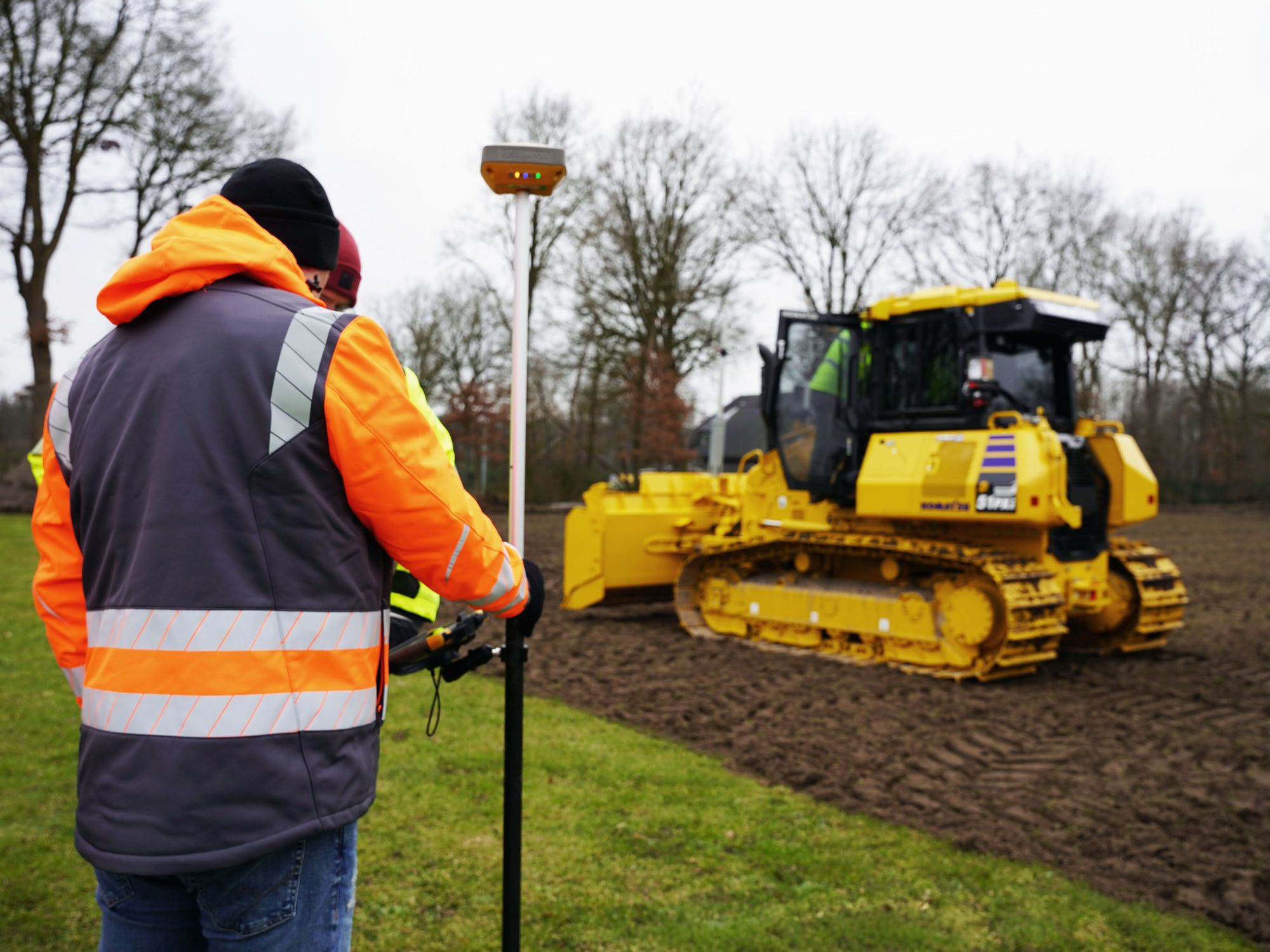 Ein gelber Komatsu-Dozer mit GNSS-Steuerung schafft ein Planum auf einer Wiese