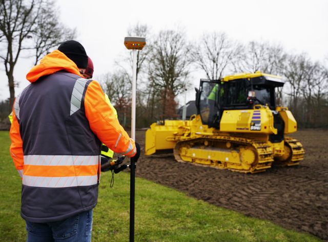 Ein gelber Komatsu-Dozer mit GNSS-Steuerung schafft ein Planum auf einer Wiese