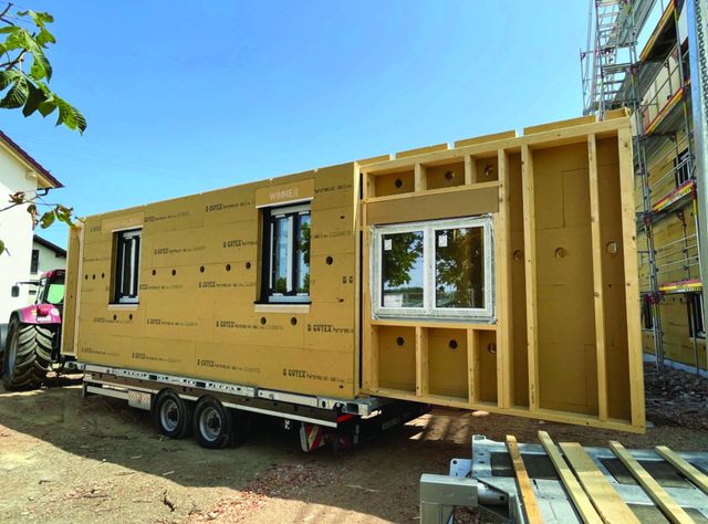 Module Holzmodulwände werden auf einem Tieflader zur Baustelle transportiert.