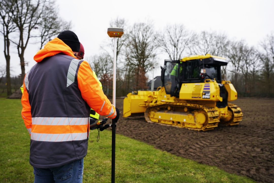 Ein gelber Komatsu-Dozer mit GNSS-Steuerung schafft ein Planum auf einer Wiese