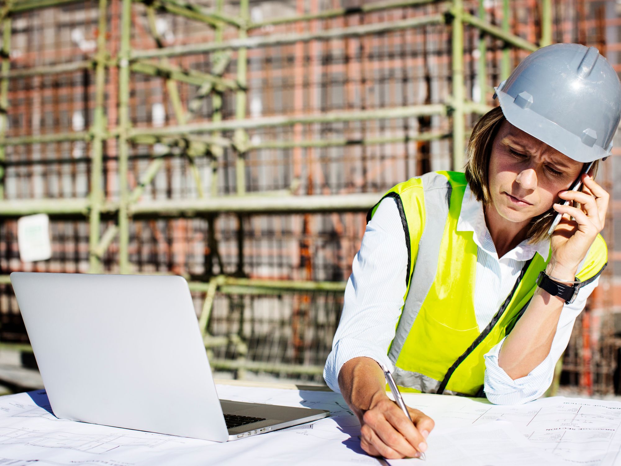 Einw Arbeiterin mit Smartphone und Laptop auf der Baustelle