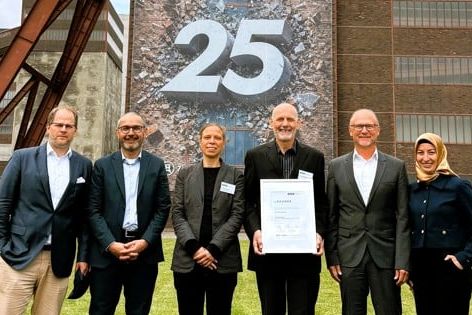 Sechs Personen (Präsidium und Geschäftsführung des VUP) stehen vor dem Förderturm der Zeche Zollverein in Essen