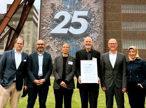 Sechs Personen (Präsidium und Geschäftsführung des VUP) stehen vor dem Förderturm der Zeche Zollverein in Essen
