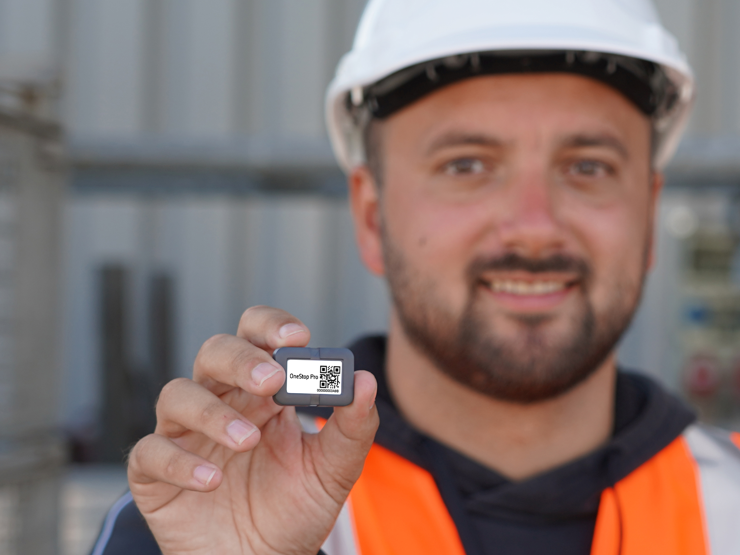 Ein Arbeiter hält lächelndt den Mini-Tracker von OneStop Pro in die Kamera