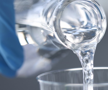 Symbolbild Trinkwasserhygiene Wasseranalytik: Hand mit Laborhandschuh gießt klares Wasser aus einer Flasche