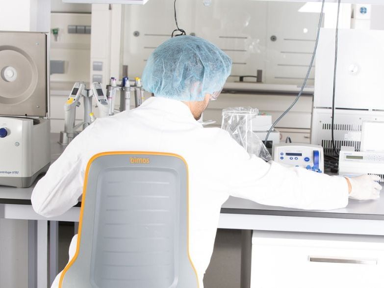Labormitarbeiter an einem Labortisch auf einem ergonomischen Laborstuhl der Marke Bimos