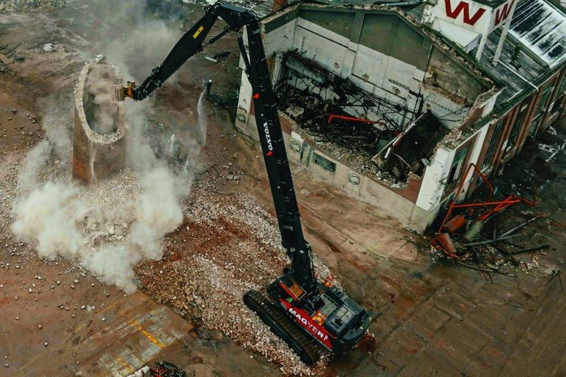 Ascendumg, Volvo CE und Epiroc - Hochleistungs-Anbaugeräte für den Abbruch Ein Volvo-Bagger reisst einen hohen Schornstein ab, der Bagger ist rot und schwarz lackiert