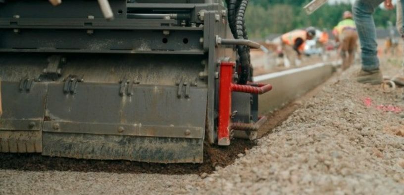 Der direkt vor der Gleitschalung positionierte Trimmer ebnet den zuvor verfestigten Untergrund, um gleichmäßige Einbauergebnisse zu gewährleisten.