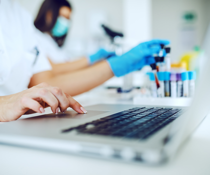 Probenröhrchen im Labor und Labormitarbeitende mit Laptop